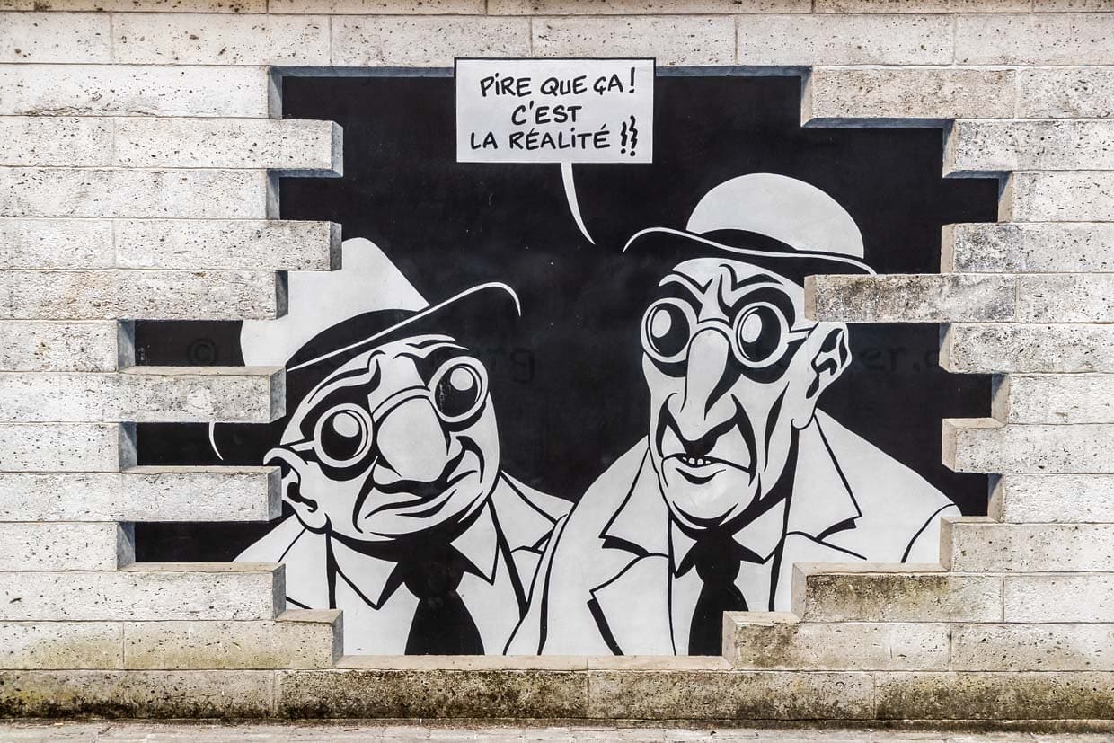 Wandgemälde aus der Serie „Réalité, Sortie de Secours” (Realität, Notausgang), die von Marc-Antoine Mathieu entworfen wurde. Es zeigt Comicfiguren mit Sprechblasen, die aus der Wand hervorzubrechen scheinen. "Sehen Sie etwas?" "Ja, schauen Sie. Es ist genau das, was ich befürchtet habe." "Was, schon wieder eine Unterwelt?" "Schlimmer als das. Es ist die Realität.". / © Foto: Georg Berg