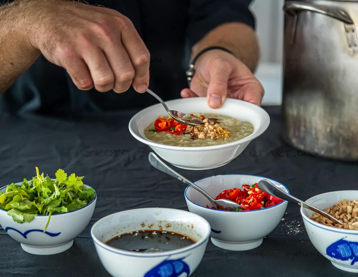 Im großen Topf befindet sich lang gekochter recht flüssiger Reis. Mit im Topf die bissfesten Fischstückchen des selbst gefangenen Wahoos. Darüber streut sich jeder nach Belieben verschiedene würzige Zutaten / © Foto: Georg Berg