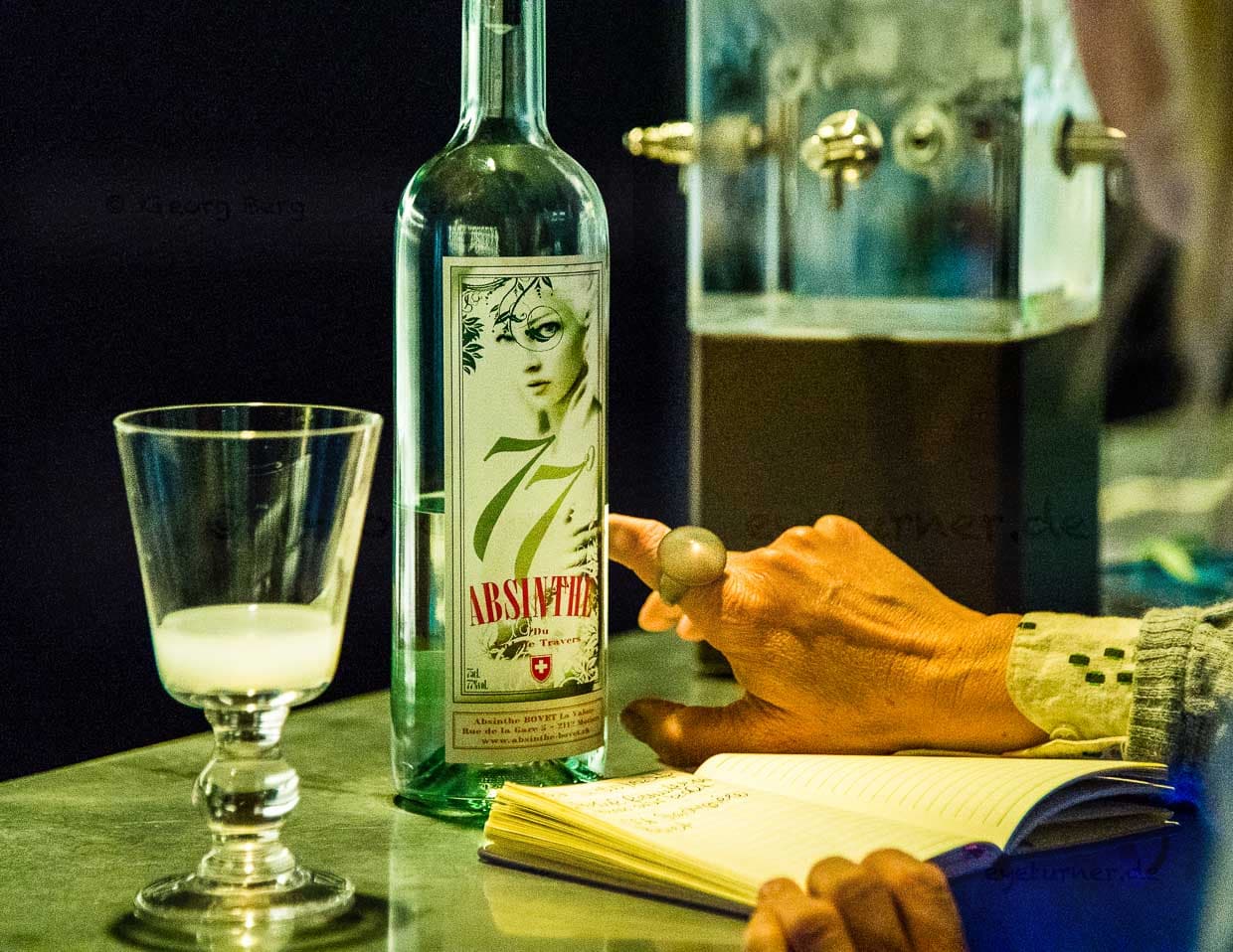 Im Maison de l’Absinthe wird man an einer Bar empfangen. Hier ist auch stets eine kalte Quelle im Einsatz. Früher tropfte das eiskalte Wasser mit der Geschwindigkeit von einem Tropfen pro Minute über den Zuckerwürfel und durch den Löffel in den zimmerwarmen Alkohol. Jeder Tropfen hinterlässt milchig-grüne Trübungen im Glas / © Foto: Georg Berg