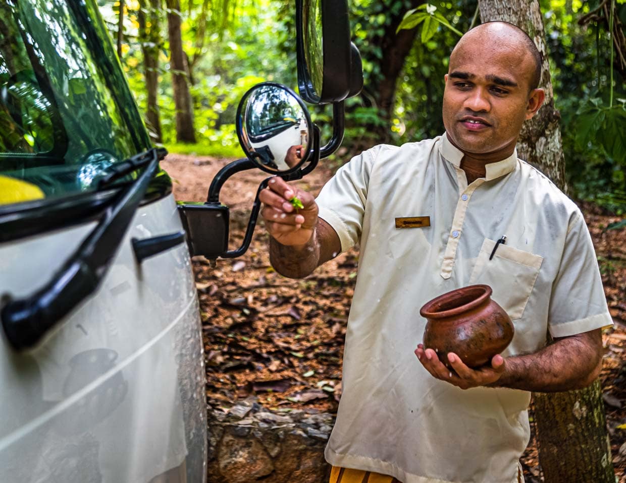 Buddhistischer Segen für eine gute Reise. Während hinten die Koffer verladen werden, sprenkelt der Hotelmanager Wasser mit Blütenblättern auf die Fahrzeugfront. Damit soll das nächste Ziel heil erreicht werden / © Foto: Georg Berg