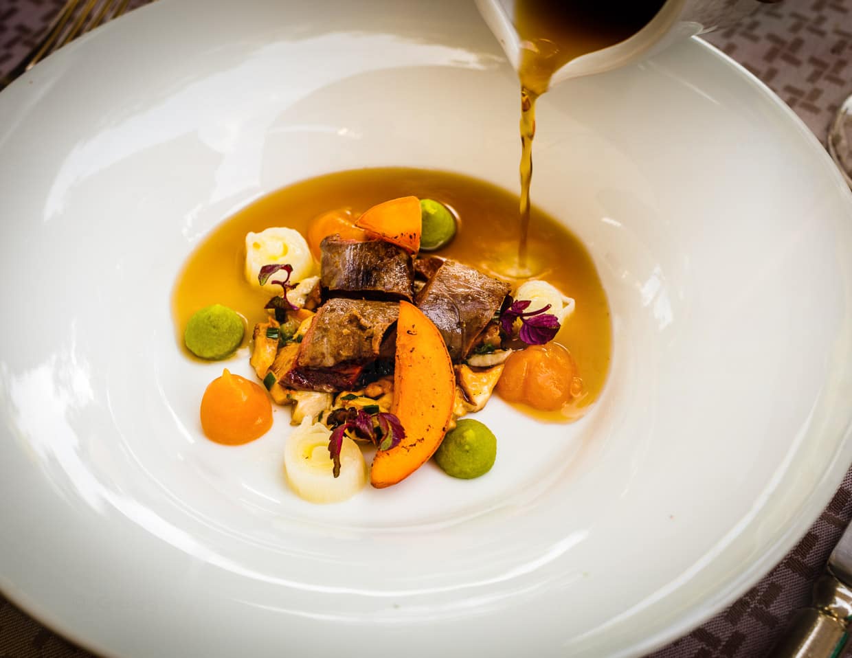 Eine Waldpilzboullion wird hier angegossen an rosa gebratenen Rehrücken, Pfifferlinge, Aprikosen und Lauch / © Foto: Georg Berg