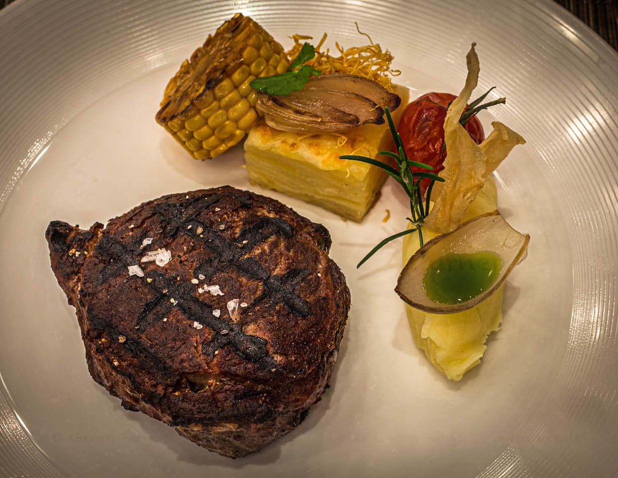 Ribeye vom Black Angus von hauseigener Weide, 28 Tage dry aged mit Kartoffelgratin und Püree mit Basilikumöl im Zwiebel-Schiffchen. Das Fleisch wird am Josper Grill zubereitet / © Foto: Georg Berg