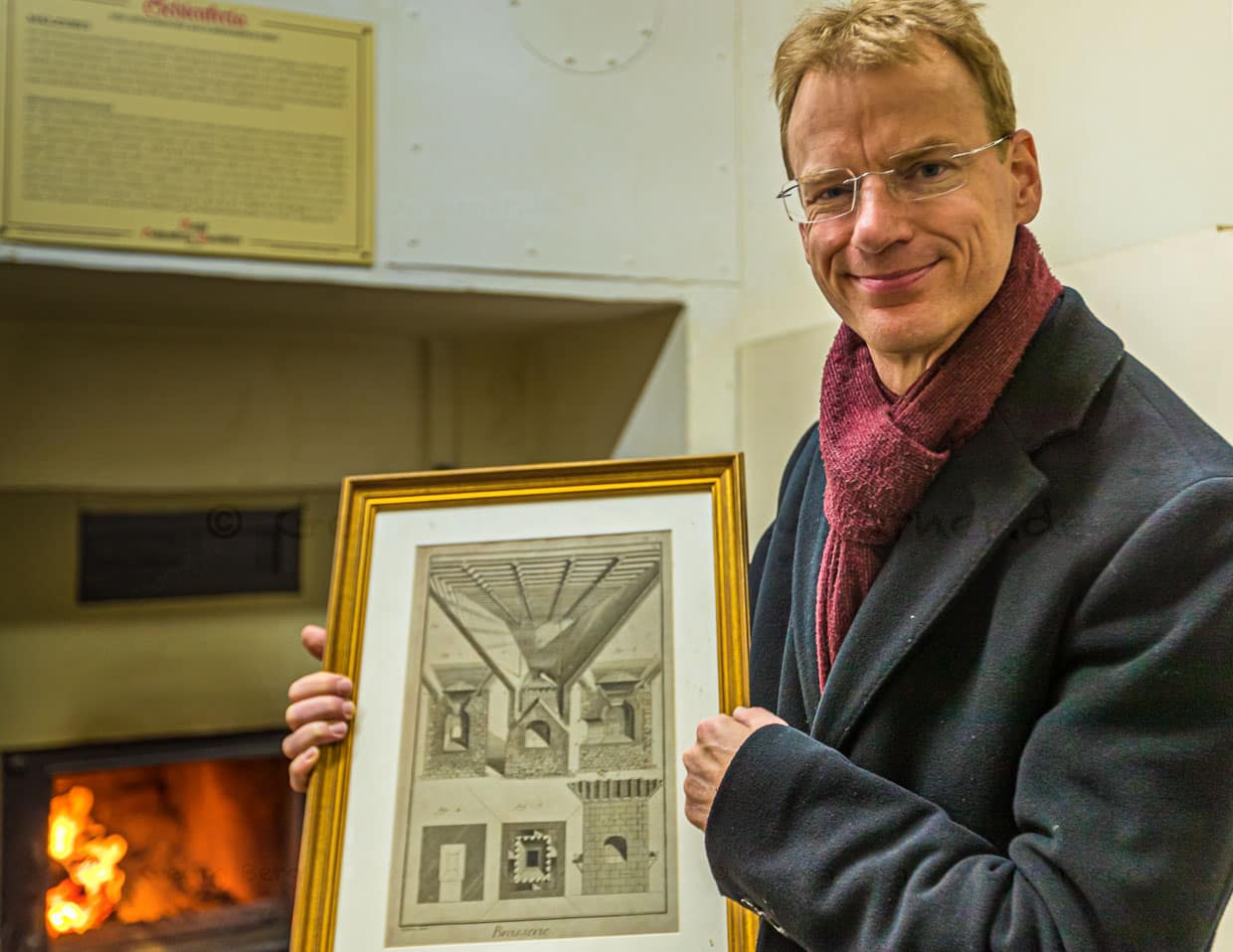 Matthias Trum von der Schlenkerla Bräu vor dem Holzofen mit dem das Grünmalz betrocknet wird. In der Hand hält er eine Zeichnung zur industriellen Malztrocknung nach Sir Nicholas Halse / © Foto: Georg Berg