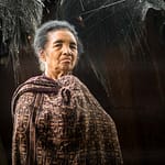 Frau in traditioneller Kleidung vor einer Hütte / © Foto: Georg Berg