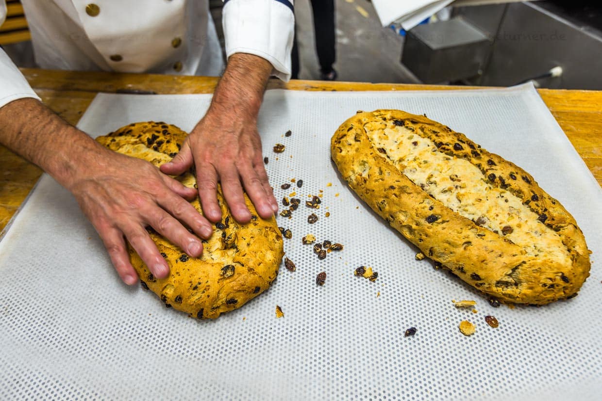 Nach dem Auskühlen beginnt die Stollenmassage. Die Sultaninen an der Oberfläche des Stollens sind verbrannt und würden den Geschmack beeinträchtigen, daher werden sie vorsichtig entfernt / © Foto: Georg Berg
