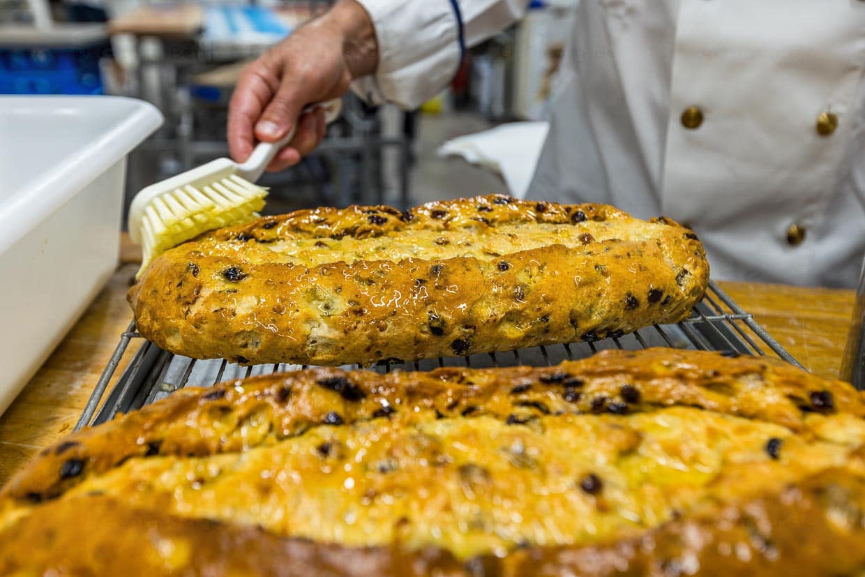 Dresdner Christstollen erhält eine natürliche Konservierung durch das Auftragen von flüssiger Butter mit einer Bürste / © Foto: Georg Berg