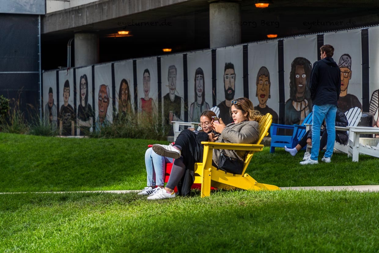 Chicago Riverwalk mit Grünflächen und Sitzmöglichkeiten. Im Hintergrund Streetart des Straßenkünstlers Dont Fret mit 55 Portraits von Chicagoern  "The People in Your Neighborhood“ / © Foto: Georg Berg