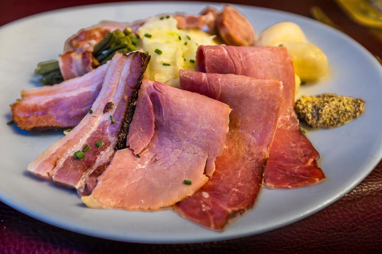 Hauptgang im Kilbi-Menü ist geräucherter Schinken (Jambon de la Borne AOP) Speck und Sauccison mit Kohl. Das Fleisch wird traditionell im Bauernkamin aufgehängt und geräuchert / © Foto: Georg Berg