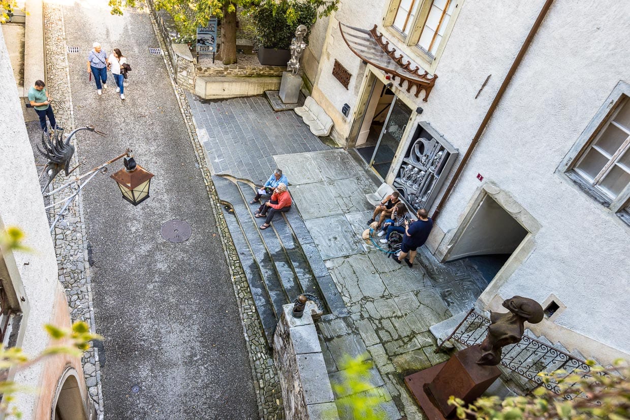 Eingang zum Museum HR Giger im Schloss St. Germain in Gruyères rechts. Im Haus links ist seit 2003 die Giger Bar untergebracht. Die Bar ist komplett in einem elfenbeinfarbenen Alien-Look gestaltet. Die Gäste sitzen auf Hakoonen-Sesseln und unter der Gewölbedecke spannen sich skelettierte Wirbelsäulen / © Foto: Georg Berg