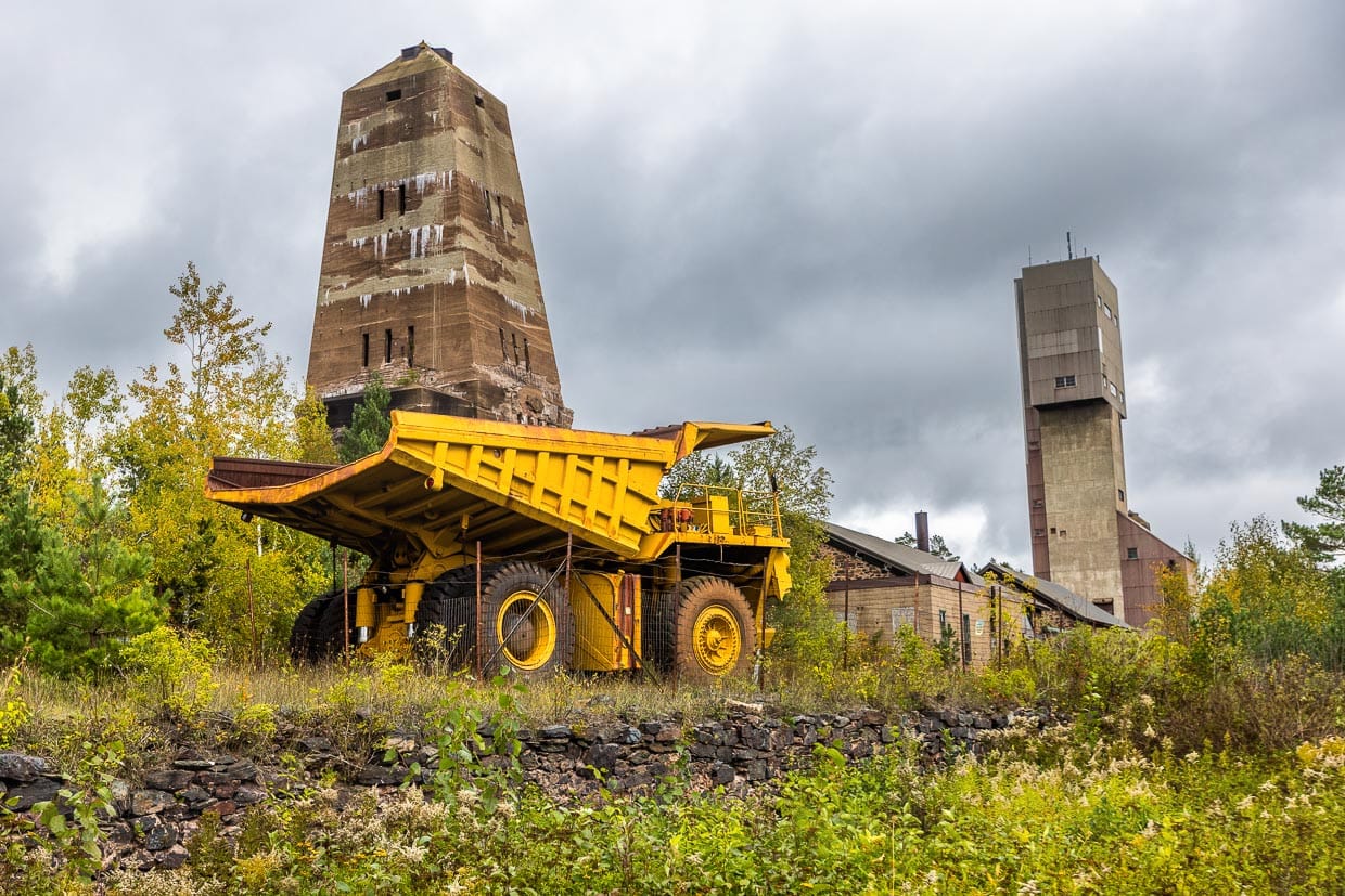 Schon 4 Meter hoch sind nur die Reifen des Erztransporters, der vor den Fördertürmen von Ishpeming ausgestellt ist. Mit ihm konnten 170 Tonnen Erz transportiert werden. Im Hintergrund der 1967 stillgelegte Förderturm in Form eines Obelisken , der vom Architekten George Washington Maher entworfen wurde und der modernere Koepe-Förderturm von 1955. Stille Zeugen des Eisenbergbaus in der Stadt Ishpeming / © Foto: Georg Berg