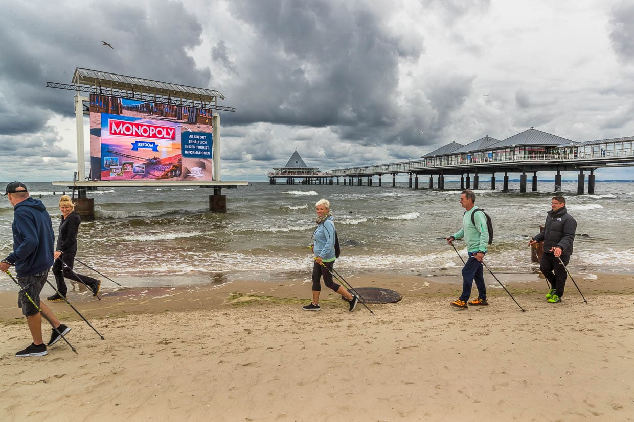 Seebrücke bei Heringsdorf mit großer Werbetafel. Holidaymakers go Nordic walking on the beach / © Photo: Georg Berg