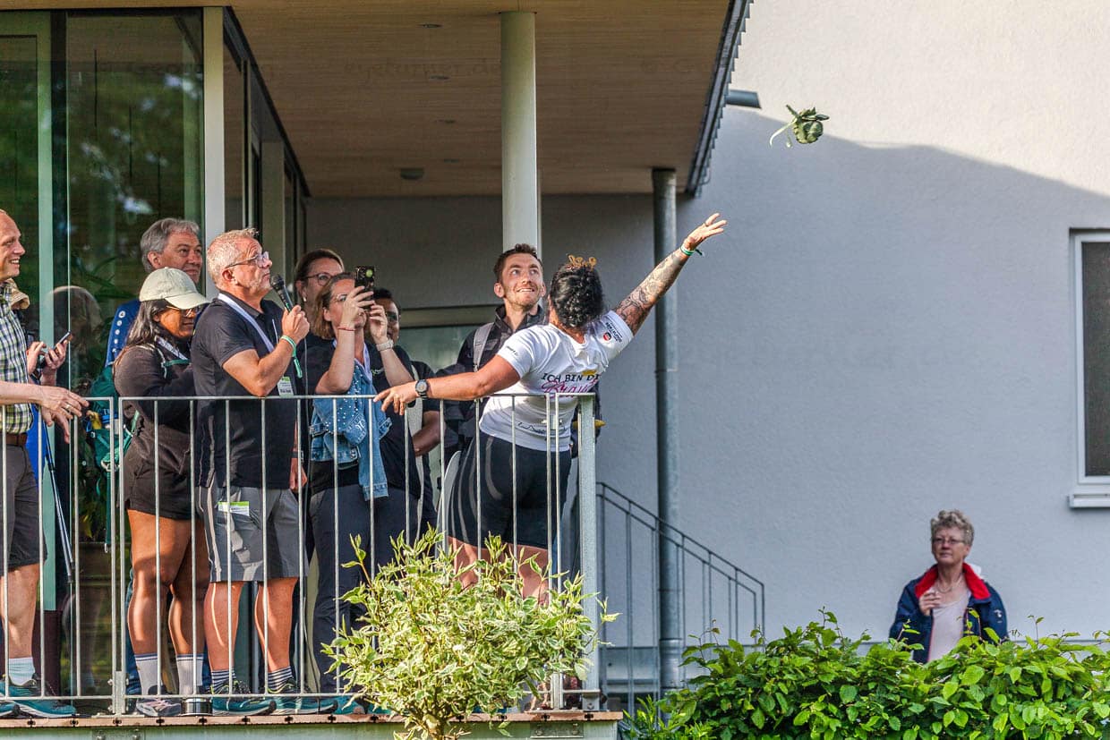 Eine Frau wirft ein kleines Bündel von einem Balkon, während eine Gruppe Menschen zuschaut in der Edwin-Trebes-Straße, Steinbach am Wald, Germany