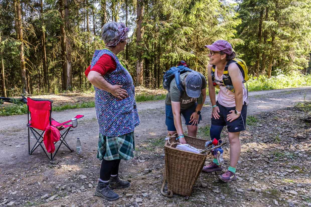 Eine ältere Frau präsentiert zwei Wanderern einen Weidenkorb auf einem Waldweg in Steinbach am Wald Germany