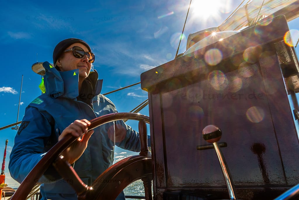 Kapitänin Jane Bothe steuert die Weisse Düne, ein holländisches Plattbodenschiff, durch das Achterwasser, die Lagune des Peenestroms, der in die Ostsee mündet. Mehrmals wöchentlich startet das Schiff von Neppermin, Wolgast oder Karlshagen zu Fahrten durchs Achterwasser / © Foto: Georg Berg