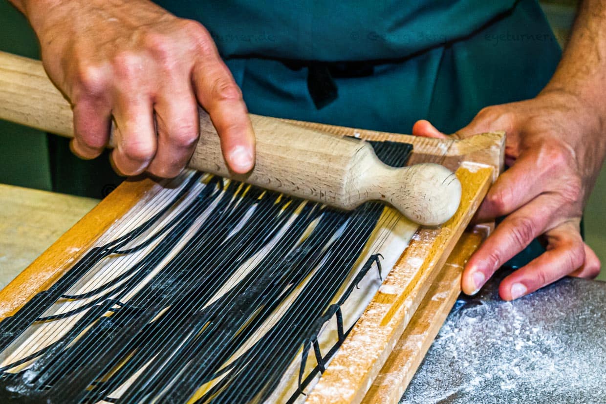 Die einzelnen Schritte der Pastaproduktion mit dem Carraturo. Zuerst wird der Teig mehrmals durch eine Nudelmaschine gedreht, bis er ganz dünn ist. Danach kann der dünne Teiglappen mit einem Nudelholz durch die Drähte gedrückt werden, die ihn in dünne Streifen schneiden. Anschließend kurz bemehlen und erst kurz vor dem Verzehr in Salzwasser al dente kochen. An der Seite des Chefkochs steht Salvatore Piacente, ebenfalls Absolvent der Kochschule Santa Maria, an der schon José Graziosi sein Handwerk lernte / © Foto: Georg Berg