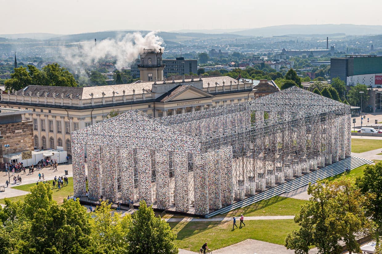 Parthenon der Bücher, der argentinischen Künstlerin Marta Minujin auf der documenta 14 in Kassel. Täglich wurde die Konstruktion, die in ihrer Dimension ein Nachbau des Tempels auf der Akropolis ist, massiver und mit weiteren Büchern bestückt. Im Hintergrund raucht die Installation "Expiration Movement" im Zwehrenturm. / © Foto: Georg Berg