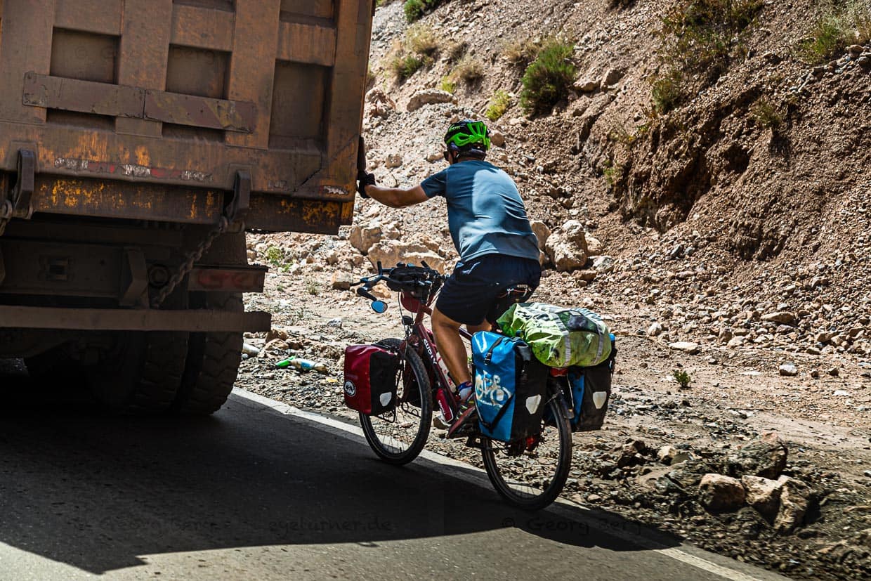 Ein Fahrradtourist lässt sich in Tadschikistan von einem LKW den Takfon-Pass hochziehen. Im Schlepptau von Transportern lassen sich gerne mehrere Hundert Höhenmeter überwinden / © Foto: Georg Berg