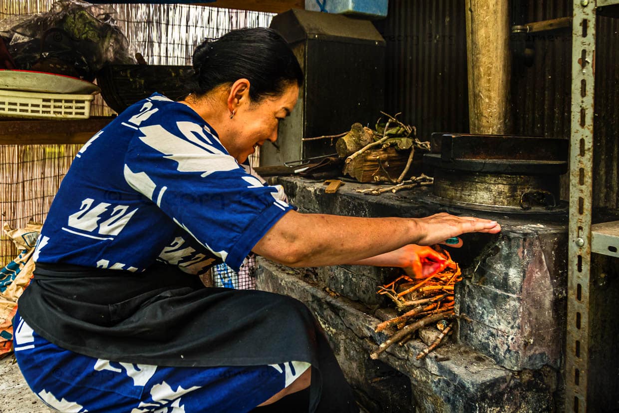 Atsuko Kato vor ihrem Holzofen. Der Reis für das Kaiseki-Menü wird über dem Holzfeuer gekocht Reis aus regionalem Anbau, serviert in handgefertigten Keramikschalen / © Foto: Georg Berg
