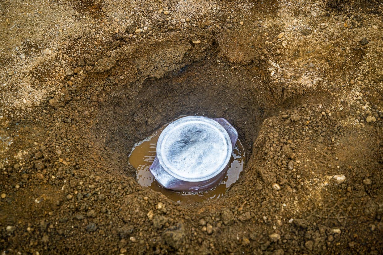 Brottopf mit Deckel und in Folie gewickelt und in einem Erdloch an den heißen Quellen von Laugarvatn. Der Topf steht in kochend heißem Wasser. Er wird mit Erde bedeckt und nach 24 Stunden wieder herausgeholt. Solange benötigt das Roggenbrot, Hverabrauð, zum Garen / © Foto: Georg Berg
