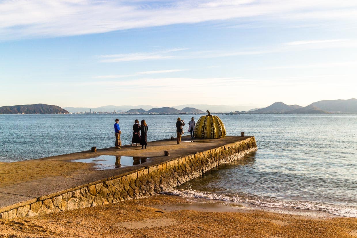 Steg mit Yellow Pumpkin von Yayoi Kusama. Der berühmtem gelbe Kürbis wurde 2021 von einem Taifun isn Meer gespült. 2022 wurde an selber stelle ein neues Exemplar aufgestellt / © Foto: Georg Berg