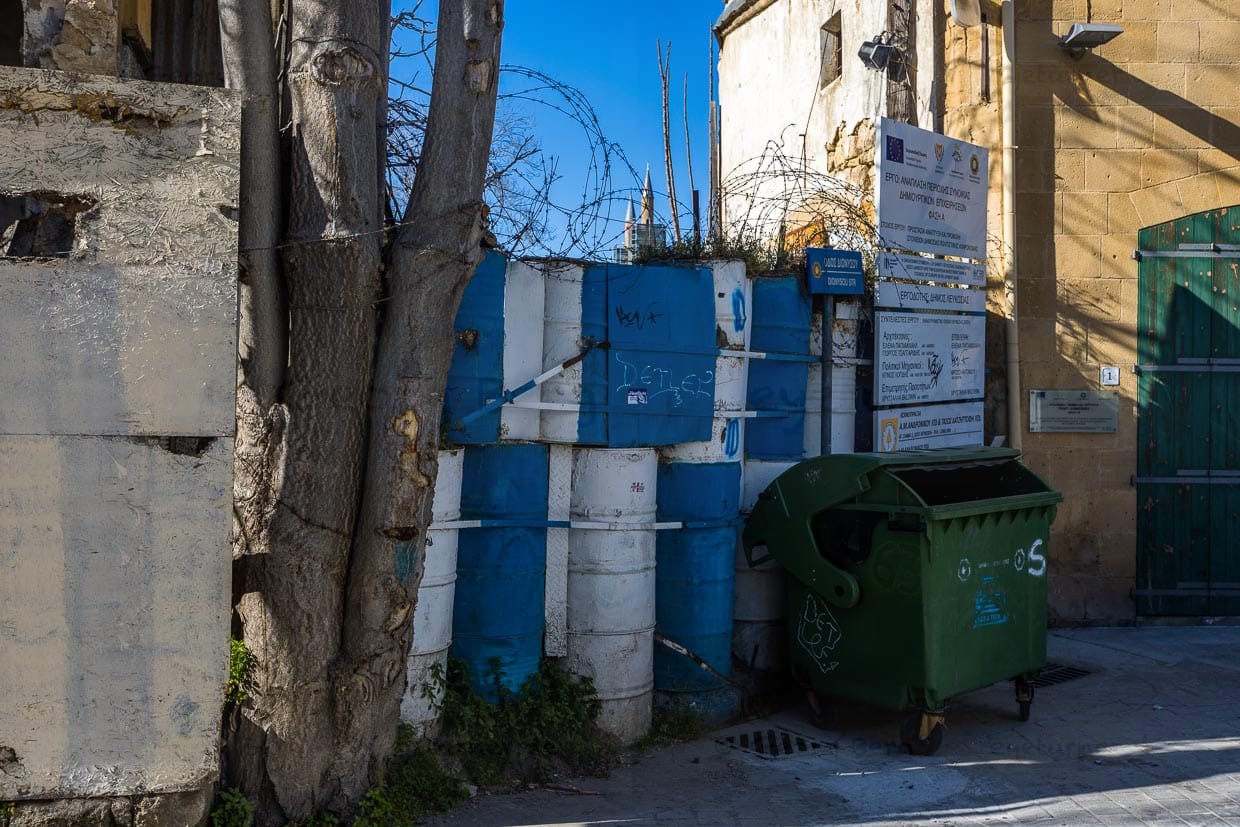 Barrikaden und Stacheldraht an der Green Line im Süden von Nikosia. Im Hintergrund sieht man die Spitzen der Minarette der Selimiye Moschee im Norden der Stadt / © Foto: Georg Berg