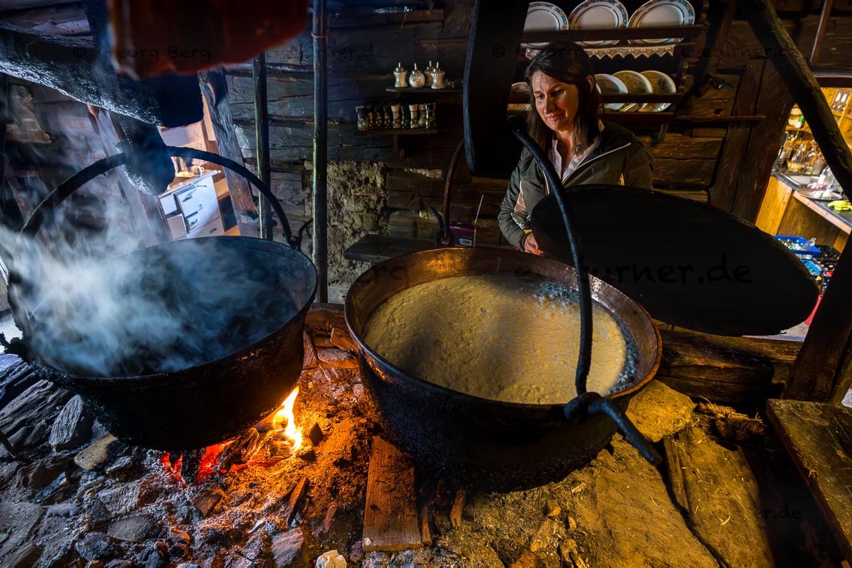 Helga Gruber, Almwirting und Bäuerin zeigt Magermilch, die in einem großen Kupferkessel, auf der 400 Jahre alten Feuerstelle aufgekocht wird. Spezialität auf der Karseggalm ist Knetkäse, der zu Kugeln geformt und über der Feuerstelle geräuchert wird / © Foto: Georg Berg