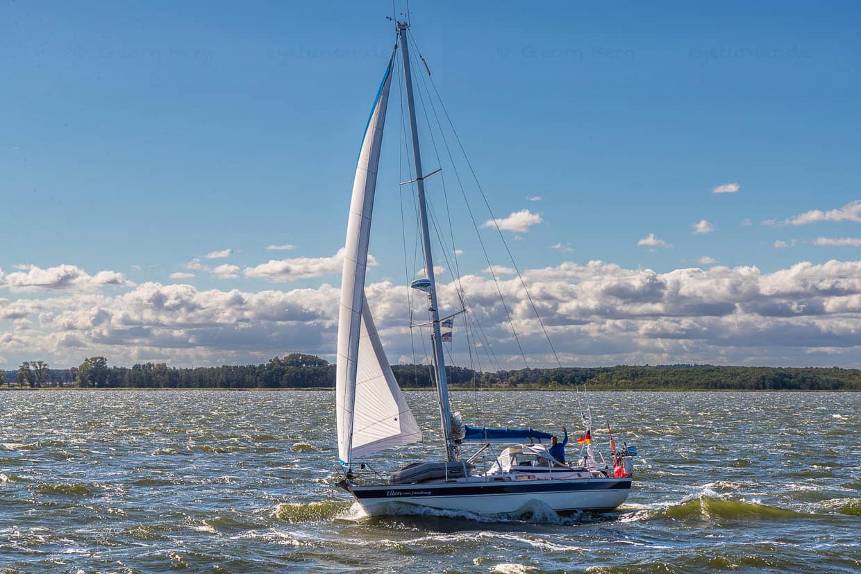 Der Skipper eines Segelbootes grüssst das Fahrgastschiff Weisse Düne bei seiner Fahrt durch die Lagune des Peenestroms, das sogenannte Achterwasser / © Foto: Georg Berg