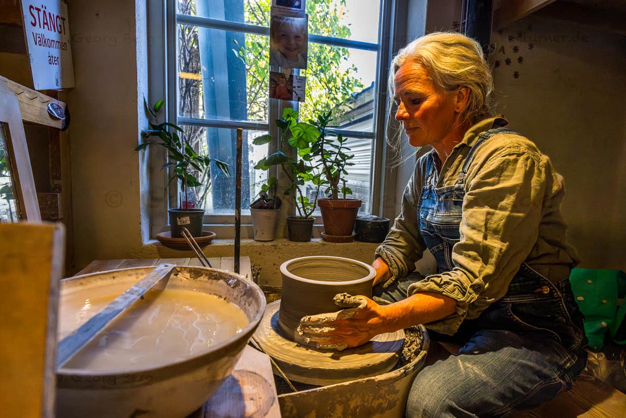 Lisa Wohlfahrt an der Töpferscheibe in ihrem Atelier in Mölle. Die Keramikwerkstatt liegt am Fuß des Kullabergs und ist bekannt für ihre handgefertigten, langlebigen Keramiken. Jedes Stück durchläuft bis zu 15 Bearbeitungsschritte, bevor es fertiggestellt wird, und ist ein Unikat. Die Produkte werden sowohl im eigenen Laden als auch für besondere Anlässe wie Hochzeiten oder Firmenaufträge gefertigt, Mölle Krukmakeri / © Foto: Georg Berg