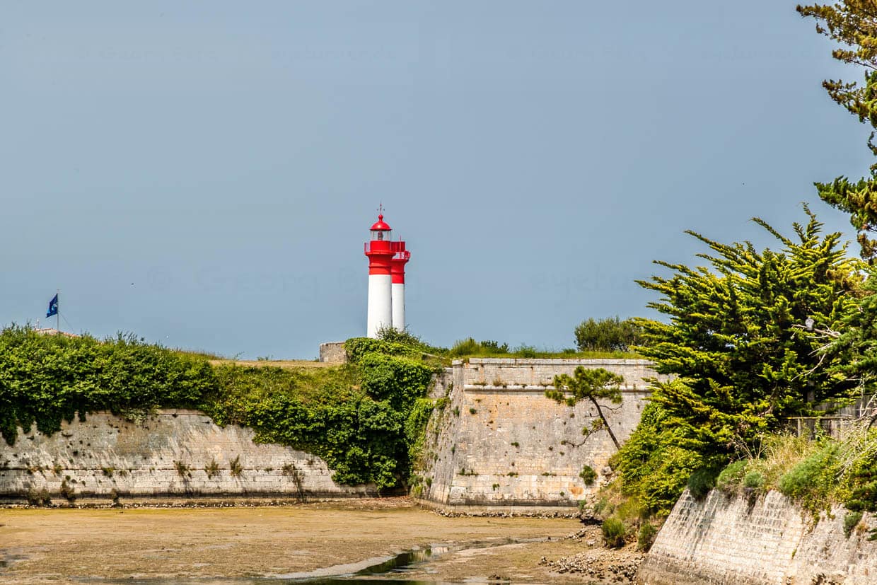 Befestigungswall der Insel Aix mit den beiden Leuchttürmen der Insel. Die Leuchttürme dienten dazu, Schiffe sicher durch die seichten und teils gefährlichen Gewässer um die Insel zu navigieren. Da die Zufahrt zum Marinearsenal von Rochefort gut geschützt und kontrolliert werden musste, wurden mehrere strategische Leuchtpunkte eingerichtet / © Foto: Georg Berg