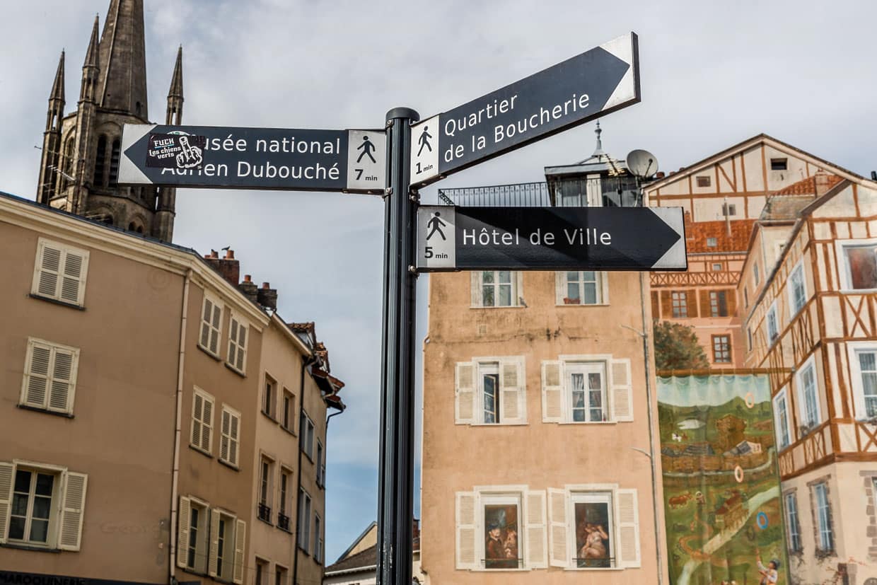 Hinweisschilder im Zentrum von Limoges, die zu den Sehenswürdigkeiten der Stadt weisen, wie das Musée National Adrien Dubouché, das Metzgerviertel und das Rathaus, im Hintergrund eine Wandmalerei, im Stil der alten Fachwerkhäuser / © Foto: Georg Berg