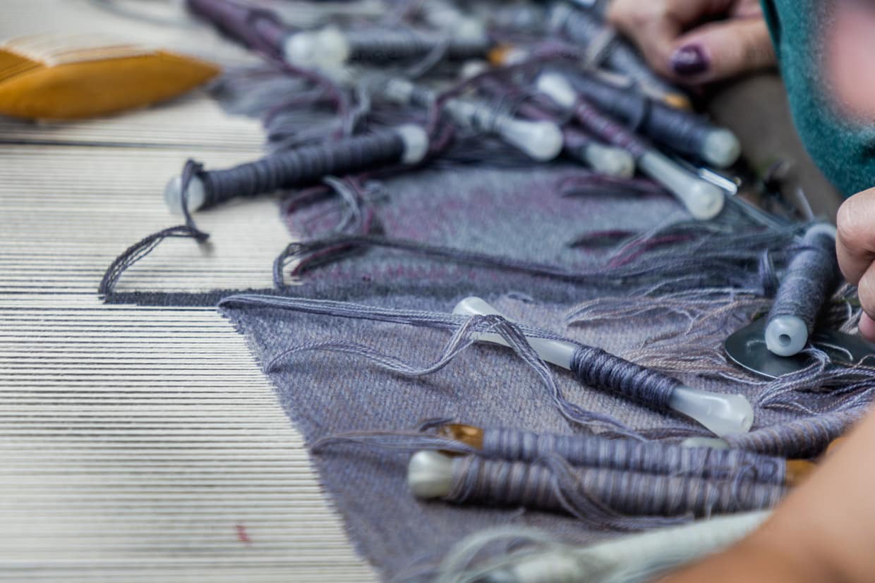 Atelier Robert Four in Aubouusson, hier wird der Wandteppich Hommage à George Sand gefertigt. Detailaufnahme mit Webschiffchen, die das Wollgarn in verschiedenen Farbnuancen tragen sowie ein Ausschnitt der Kette, gespannten Längsfäden im Webstuhl, durch die das Schiffchen mit dem Webgarn geführt wird / © Foto: Georg Berg