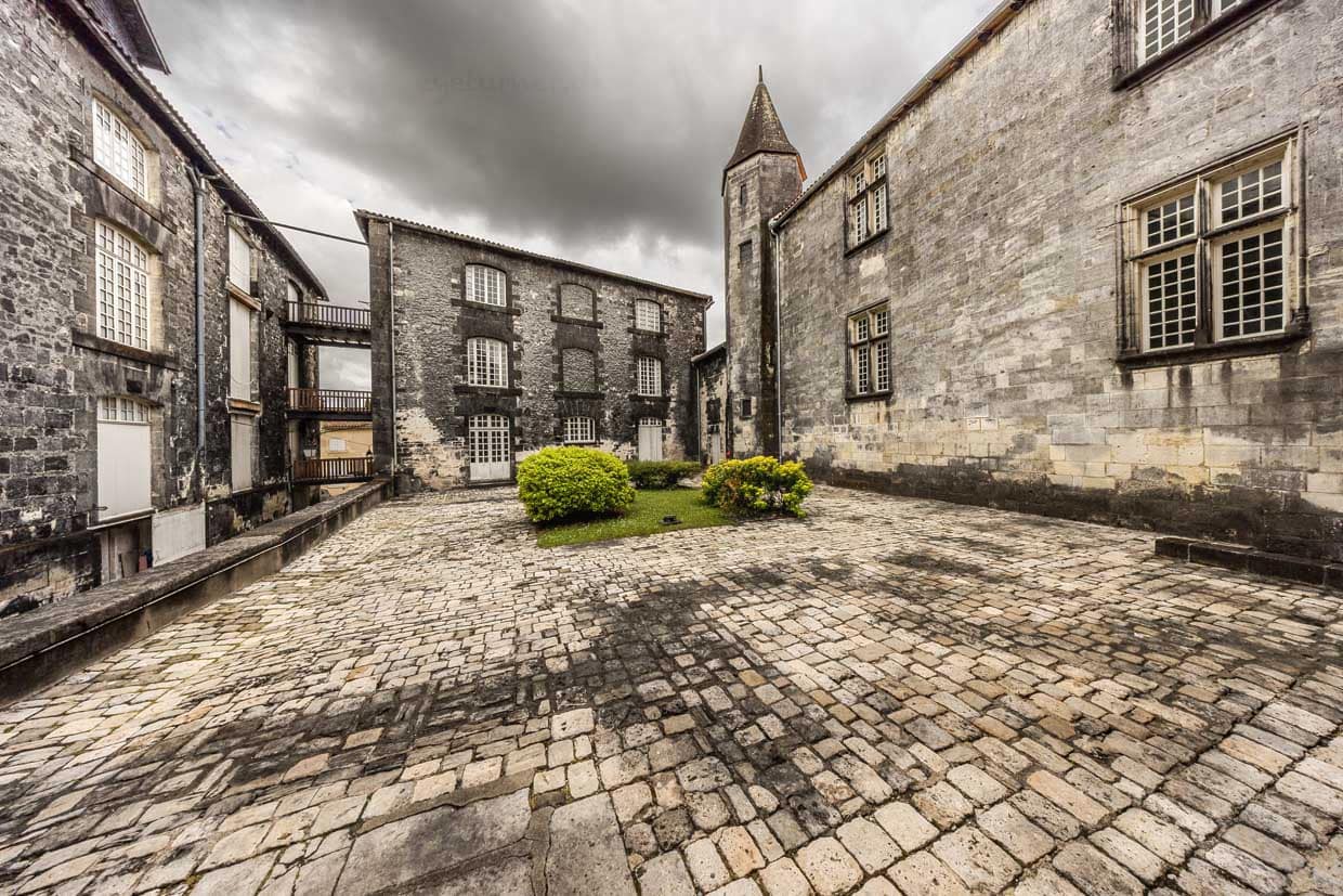 Innenhof Schloss Cognac. Der schwarze Pilz ist in Cognac so charakteristisch, dass sogar die weißen Kalksteinfassaden der Stadt und die Reifekeller („chais“) durch ihn dauerhaft geschwärzt sind. Die Schwarzfärbung der Kellerwände ist ein direktes Resultat der Spirituosenherstellung und ein sichtbares Zeichen der langen Cognac-Tradition / © Foto: Georg Berg