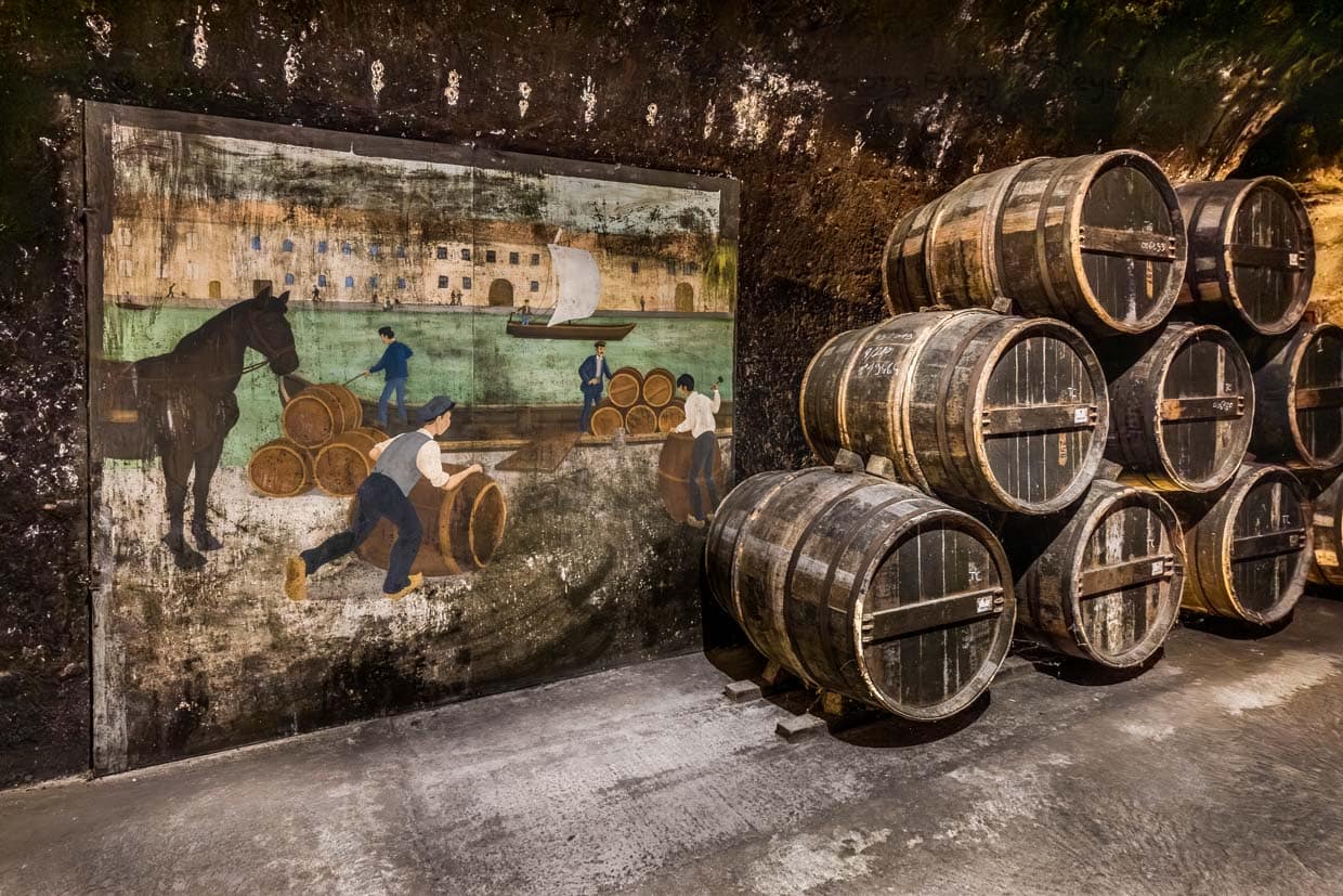 Alte Cognac-Fässer in der Lagerräumen von Schloss Cognac. Daneben eine Gemälde, auf dem der Handel mit Cognac und Transport über den Fluss Charente dargestellt wird / © Foto: Georg Berg