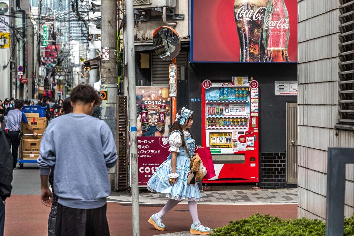 Junge Frau in Osaka im durchgestylten Dirndl-Look mit großer Handtasche in Form eines Plüschteddys. Im Hintergrund Getränkeautomaten / © Foto: Georg Berg