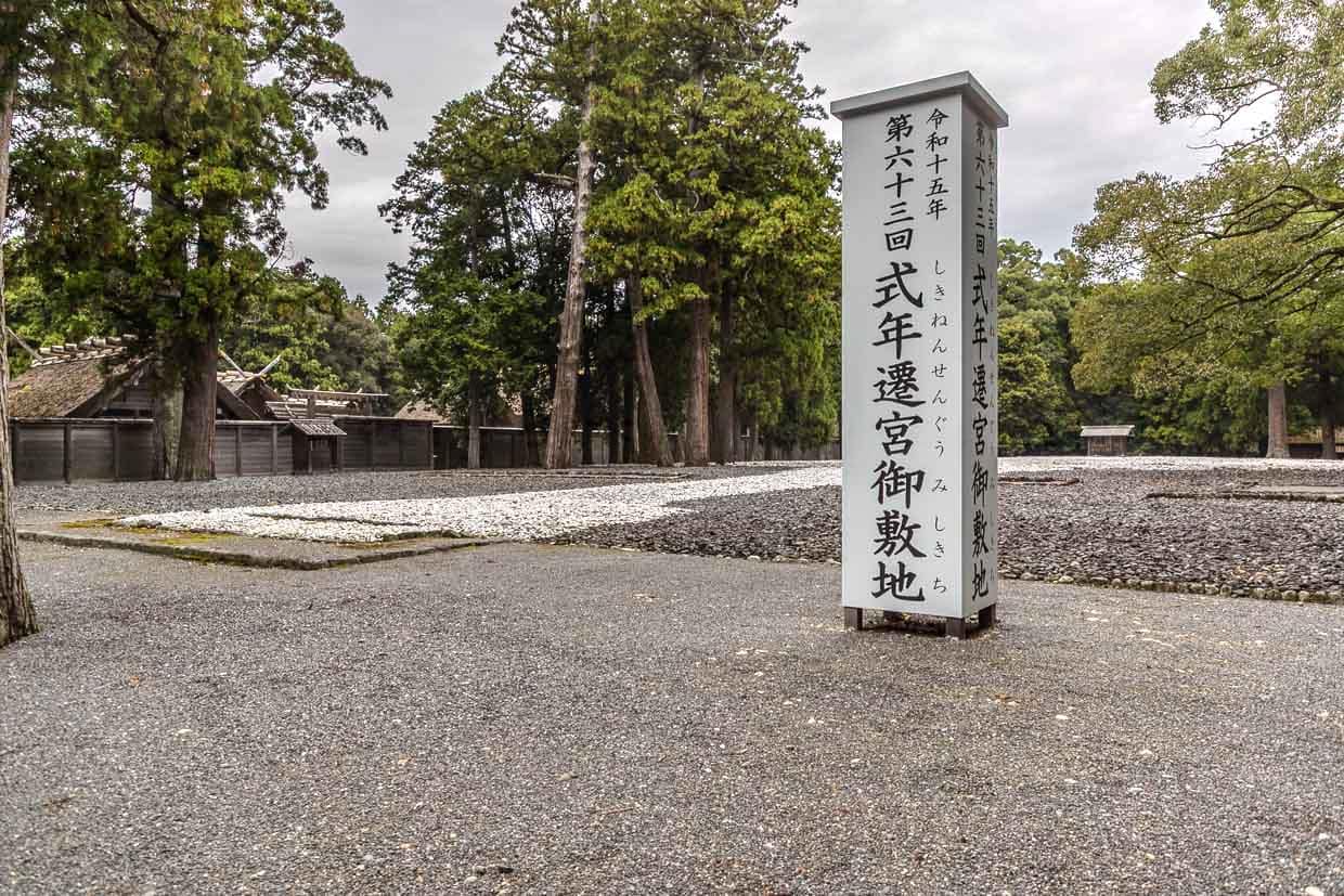 Japanisches Schild steht auf Kiesfläche vor traditionellen Holzhäusern und Bäumen in Miyajiri 1-chome, Ise, Japan