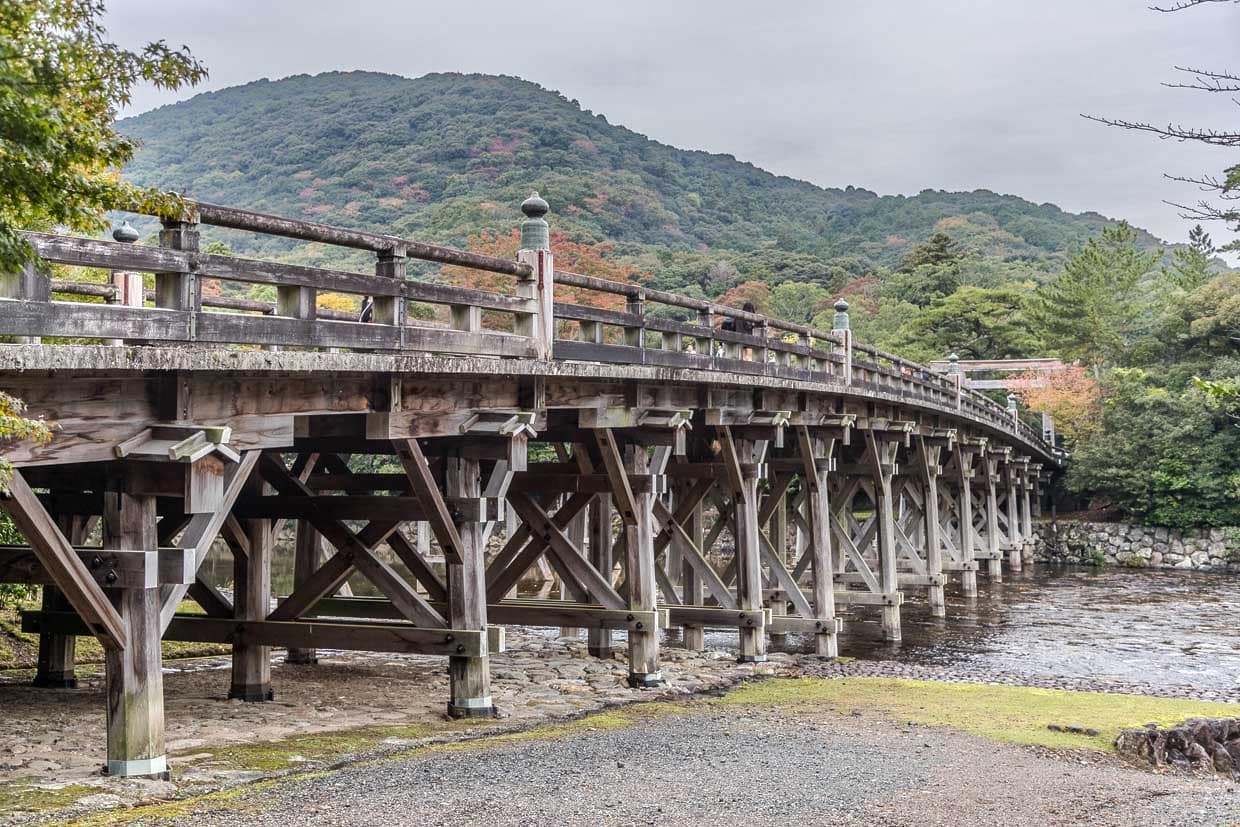 Die historische hölzerne Fire bridge überspannt einen Fluss vor einer bewaldeten Hügellandschaft in Ise, Japan