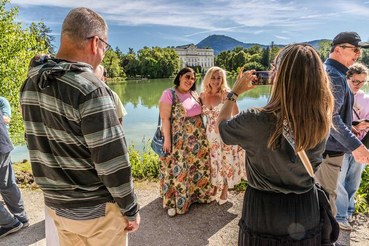 Eine Frau fotografiert zwei lächelnde Frauen vor einem See und Schloss Leopoldskron an der König-Ludwig-Straße Salzburg Austria