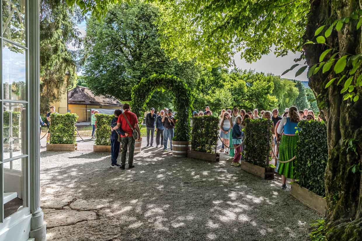 Eine Gruppe Menschen steht auf einem Kiesweg unter einem grünen Bogen und Bäumen am Fürstenweg, Salzburg, Austria
