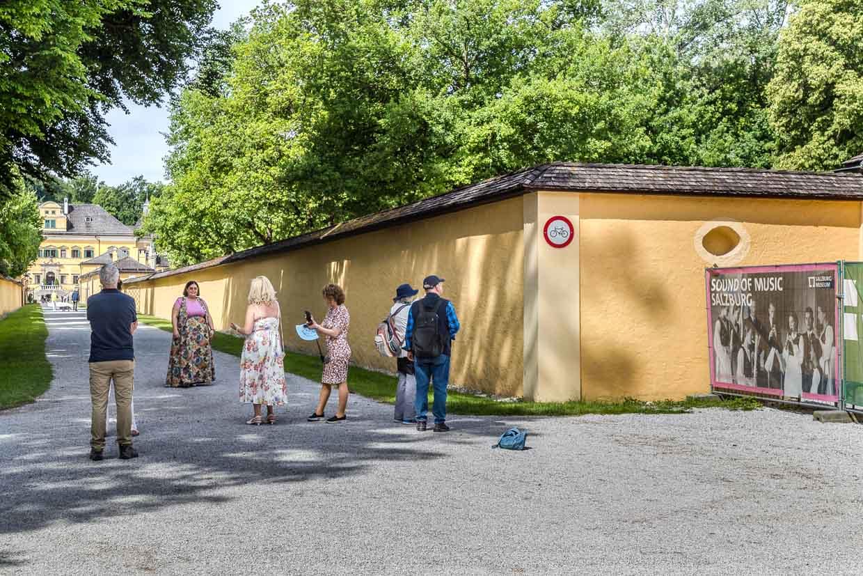 Besucher spazieren auf dem Fürstenweg in Salzburg Austria entlang einer gelben Mauer und einem historischen Schloss mit Sound of Music Banner