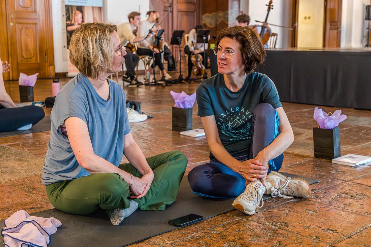 Zwei Frauen unterhalten sich während einer Veranstaltung auf Yogamatten am Domplatz, Salzburg, Austria, mit Live-Musik
