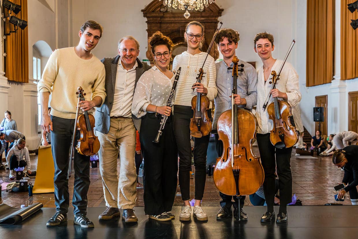 Ein Musikensemble aus jungen Musikern und einem älteren Mann posiert lächelnd mit Violinen, Cello und Klarinette in der Franziskanergasse, Salzburg, Austria