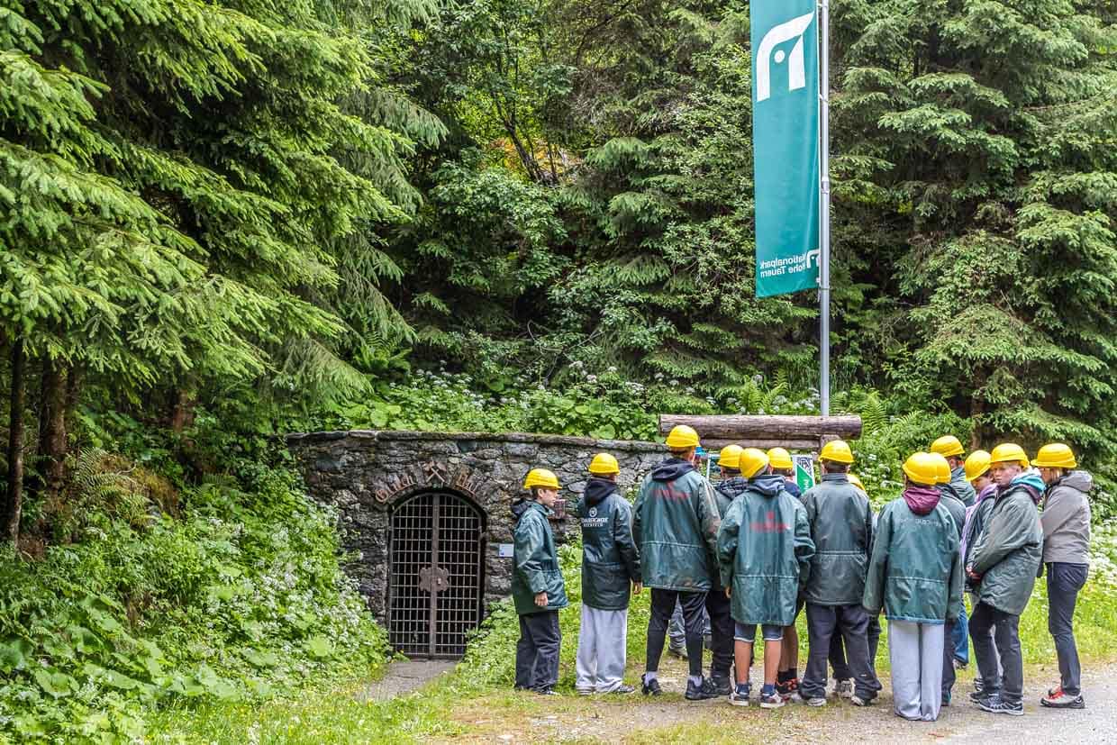 Besucher mit Helmen und Schaubergwerk-Jacken stehen vor dem Stollen "Glück Auf" am Wasserfallrundweg Untersulzbach Rosental Austria