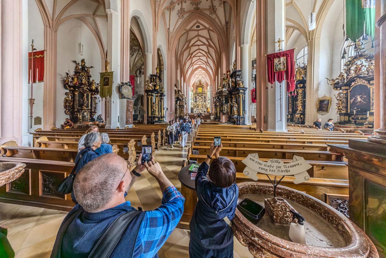 Besucher bewundern und fotografieren das historische Kirchenschiff mit prunkvollen Altären und hohen Gewölben in Poststraße Schlößl Austria