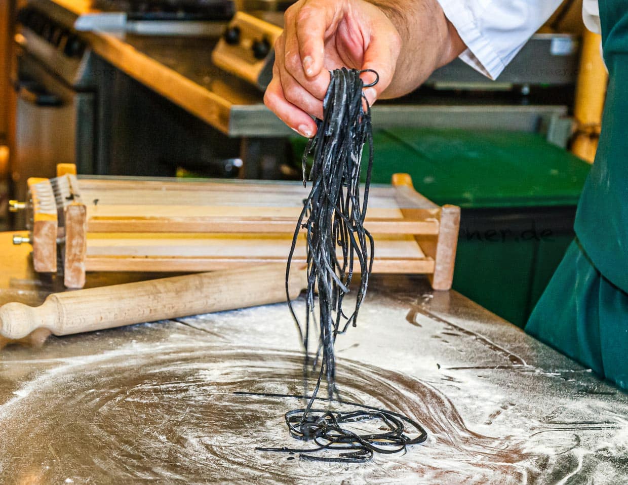 Die einzelnen Schritte der Pastaproduktion mit dem Carraturo. Zuerst wird der Teig mehrmals durch eine Nudelmaschine gedreht, bis er ganz dünn ist. Danach kann der dünne Teiglappen mit einem Nudelholz durch die Drähte gedrückt werden, die ihn in dünne Streifen schneiden. Anschließend kurz bemehlen und erst kurz vor dem Verzehr in Salzwasser al dente kochen. An der Seite des Chefkochs steht Salvatore Piacente, ebenfalls Absolvent der Kochschule Santa Maria, an der schon José Graziosi sein Handwerk lernte / © Foto: Georg Berg