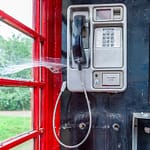 Eine traditionelle rote Telefonzelle in einer ländlichen Umgebung im Vereinigten Königreich zeigt ein Spinnennetz über dem Hörer / © Foto: Georg Berg