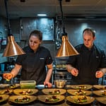 Mit Standfestigkeit und ruhiger Hand: Martina und Gavin richten in der Kombüse trotz Seegang das Hauptgericht an / © Foto: Georg Berg