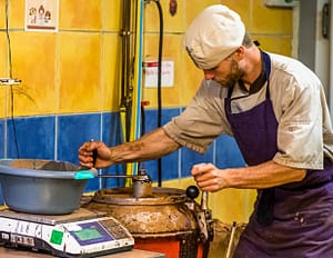 Ein Mitarbeiter der Chocolaterie Frigoulette verschließt den Mélangeur, in dem die abgewogenen Zuten gemischt und erwärmt werden. Bei Frigoulette werden keine tierischen Fette wie Milch, Sahne oder Butter verarbeitet. Auch Palmöl kommt nicht zum Einsatz. Stattdessen 68 prozentiger Kakaoanteil und echte Kakaobutter aus São Tomé / © Foto: Georg Berg