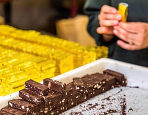 In Handarbeit wird der Bestseller der Schokoladen-Manufaktur Frigoulette in goldenes Papier verpackt. Die Malakoff Praline der Chocolaterie Frigoulette ist in ganz Frankreich erhältlich und besonders beliebt zu Weihnachten. Malakoff gehört zu den geschnittenen Pralinen, die ohne eine zusätzliche Hülle um den Kern auskommen. Die gerösteten Haselnüsse verleihen der Praline eine knusprige Konsistenz / © Foto: Georg Berg