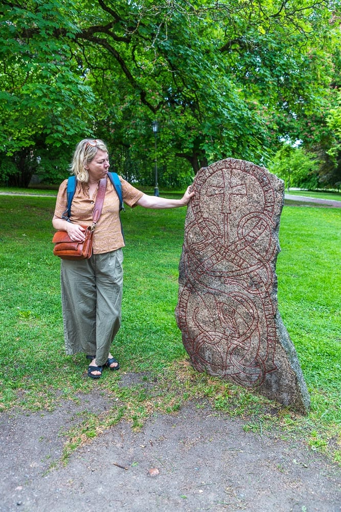Im Universitätspark von Uppsala stehen zahlreiche original Runensteine. Stadtführerin Katja Jahn erklärt, dass Runensteine zum Gedenken an jemanden von dessen Familie aufgestellt wurden. Die Inschrift nennt den Namen und die Taten des Verstorbenen sowie den Namen des Auftraggebers und des Handwerkers, der den Stein bearbeitet hat / © Foto: Georg Berg