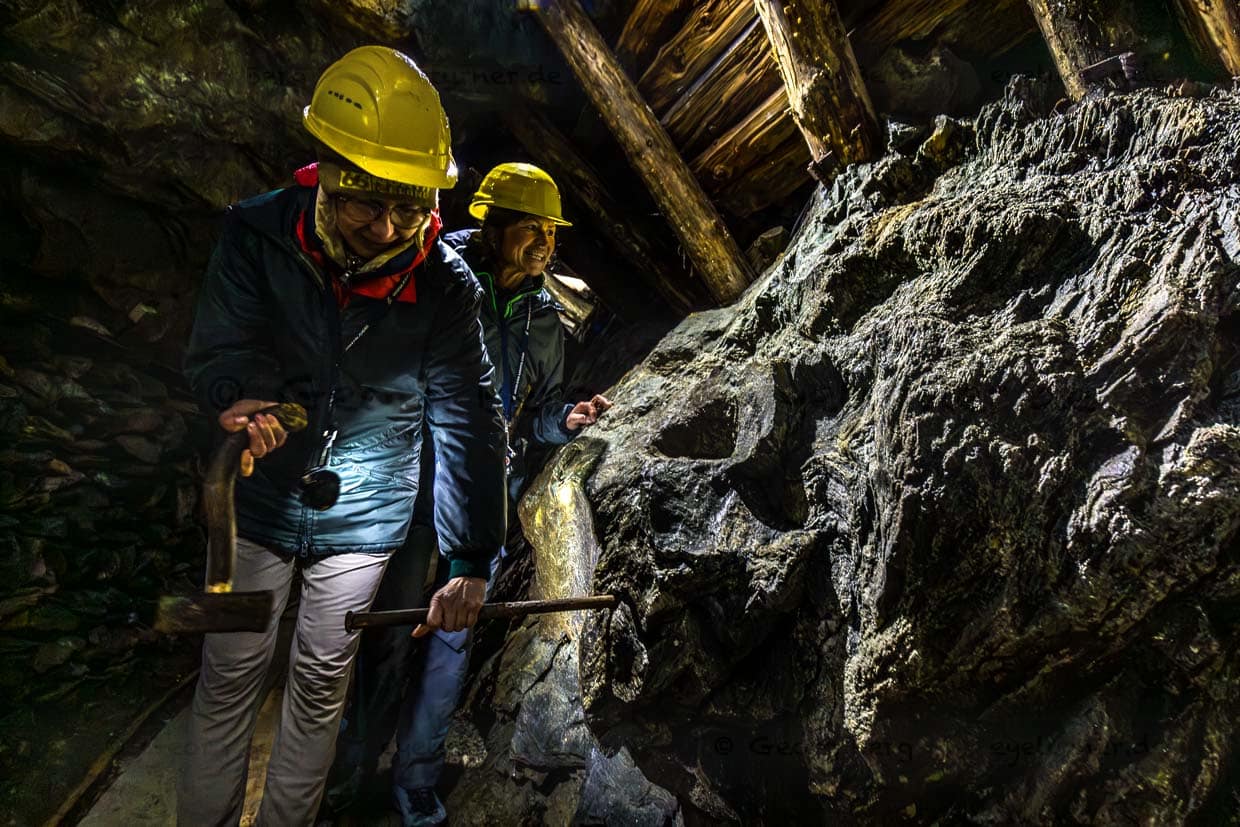 Zwei Personen mit Schutzhelmen erkunden einen Stollen mit Werkzeugen am Wasserfallrundweg Untersulzbach, Rosental, Austria